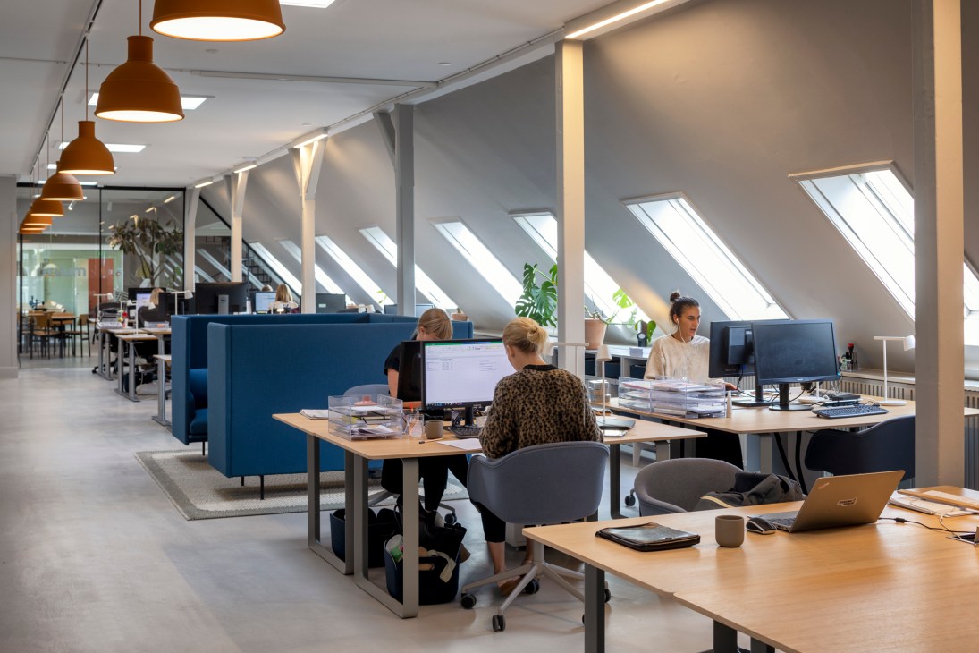 Modern open office space with skylights, pendant lamps, and employees working at wooden desks with blue dividers