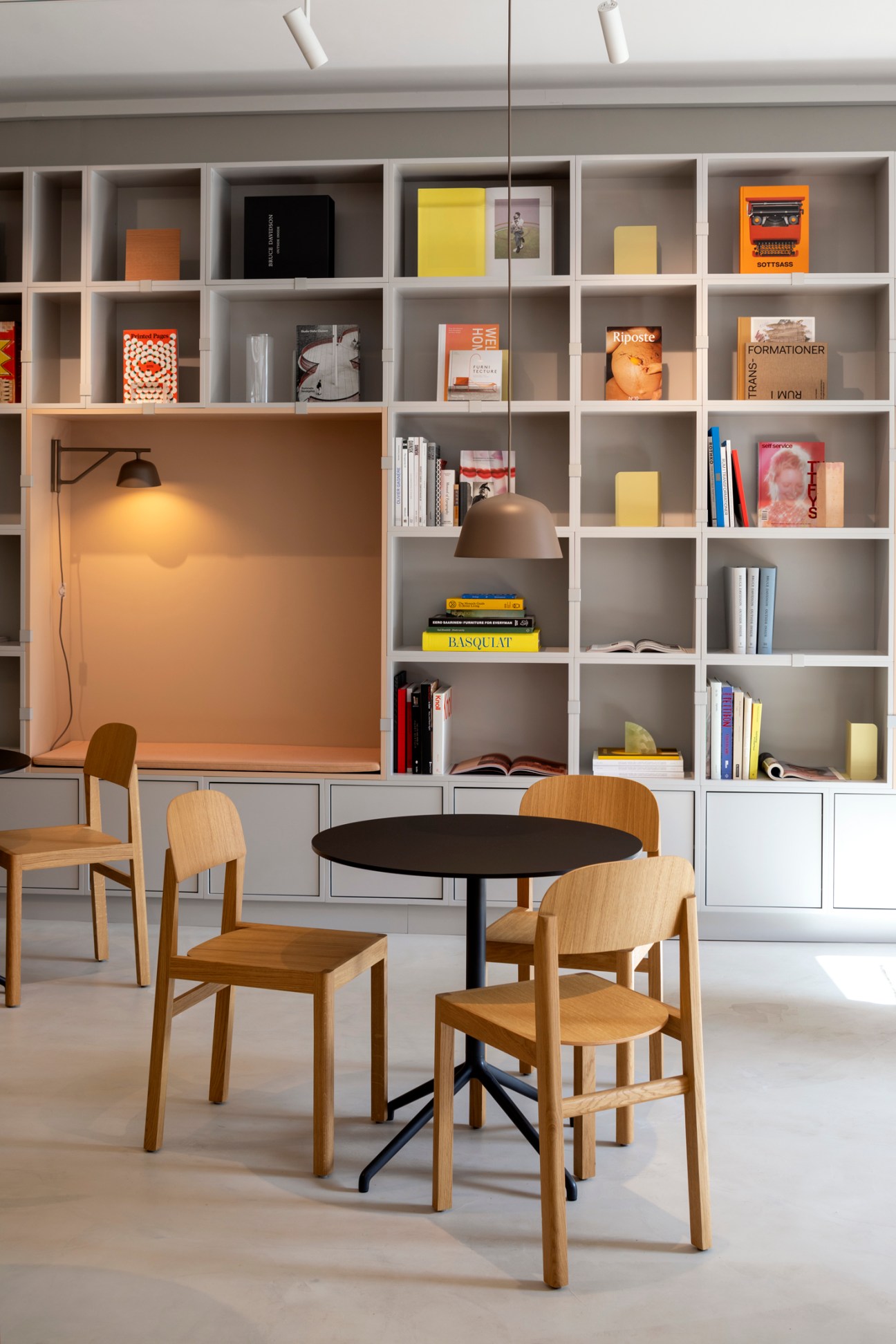 Modern library workspace with built-in white shelving, wooden chairs around black table, and task lighting