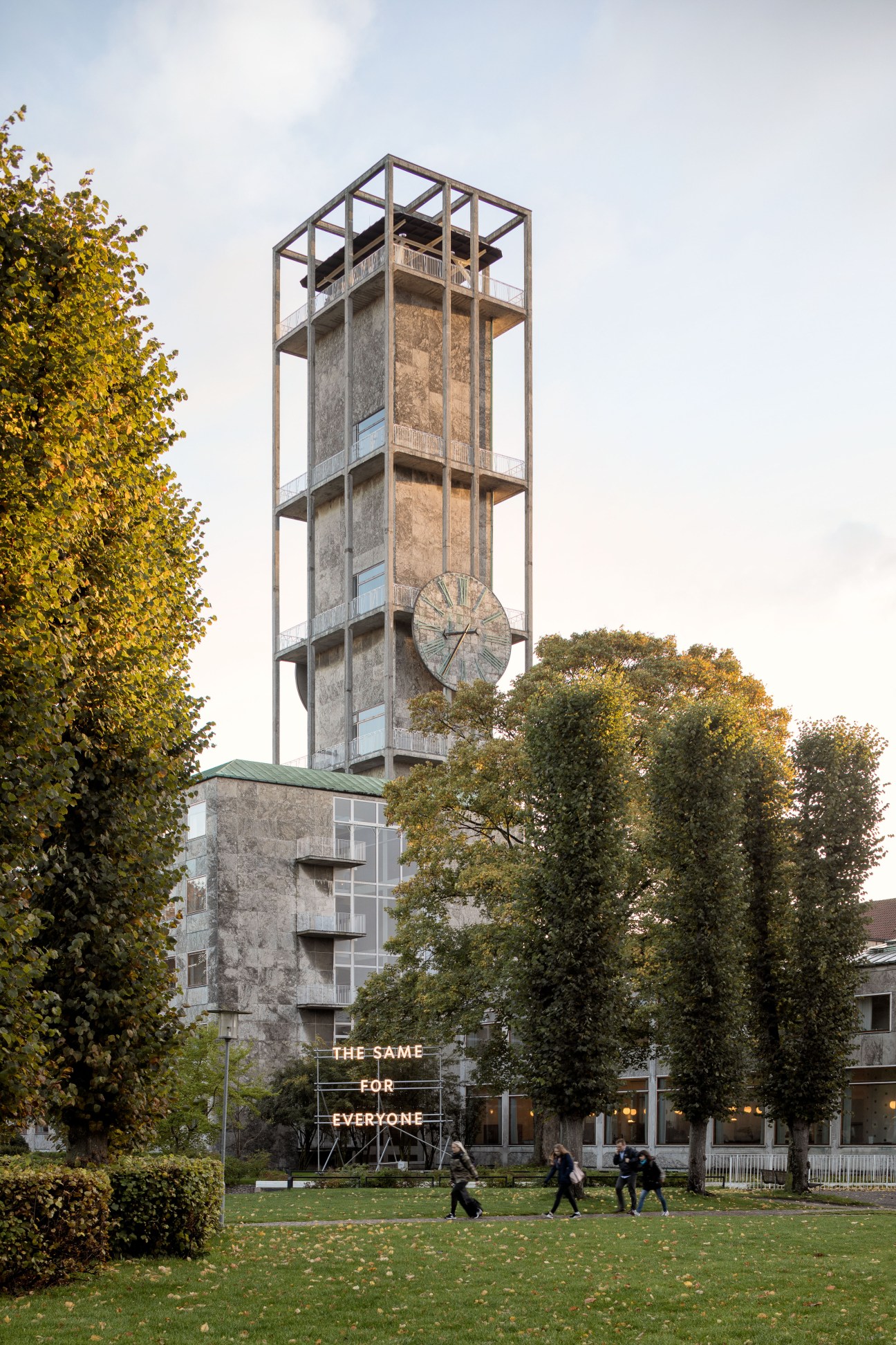 Aarhus city hall's refurbished clock tower with geometric steel frame and clock face, surrounded by autumn foliage.
