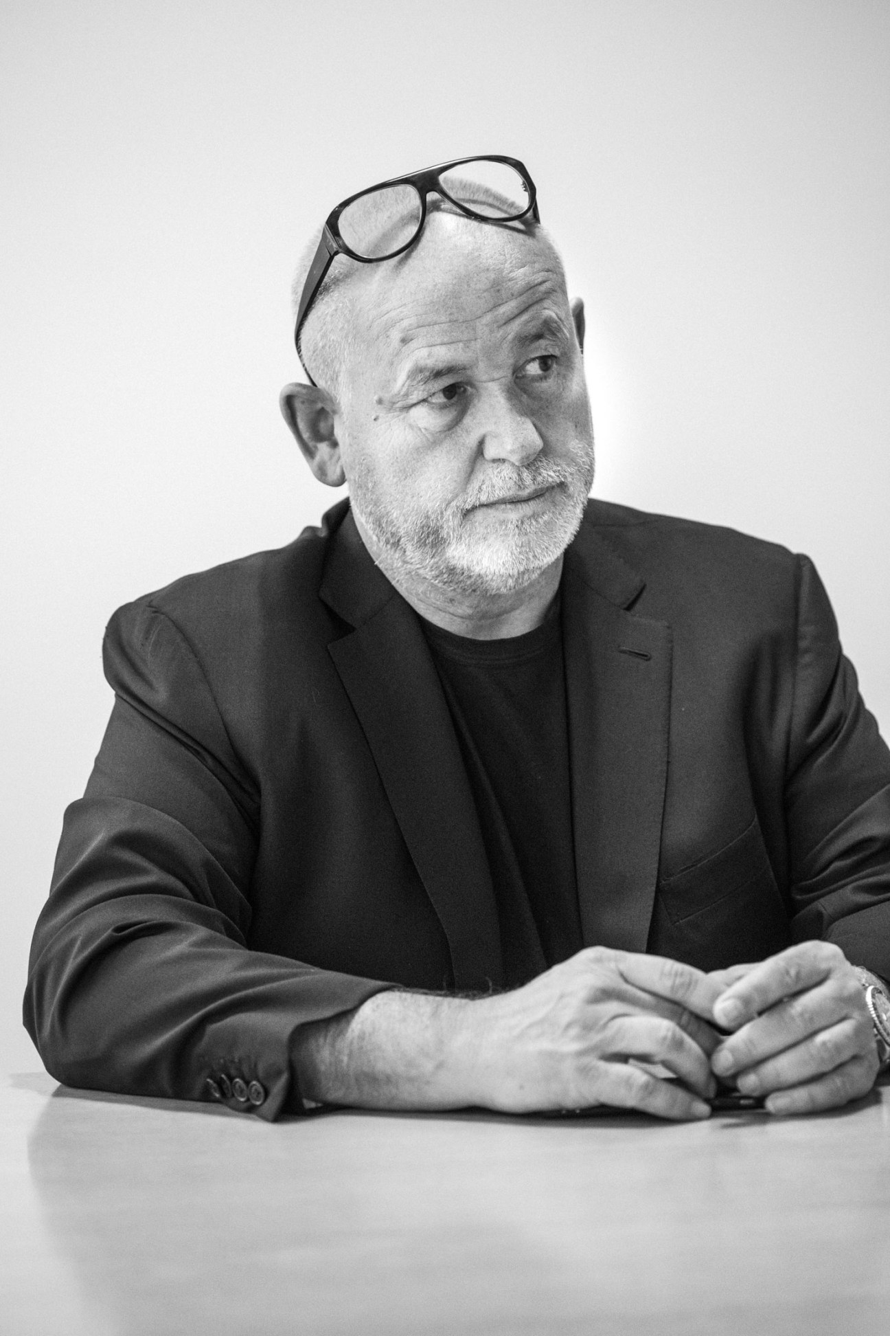 Black and white portrait of Fabien Baron wearing a dark blazer and black shirt, with glasses pushed up on his head.