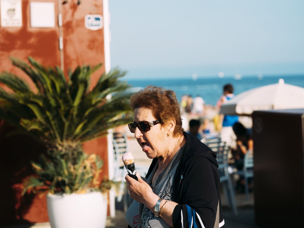 Woman eating ice cream cone at a seaside café with terracotta building and palm plants visible