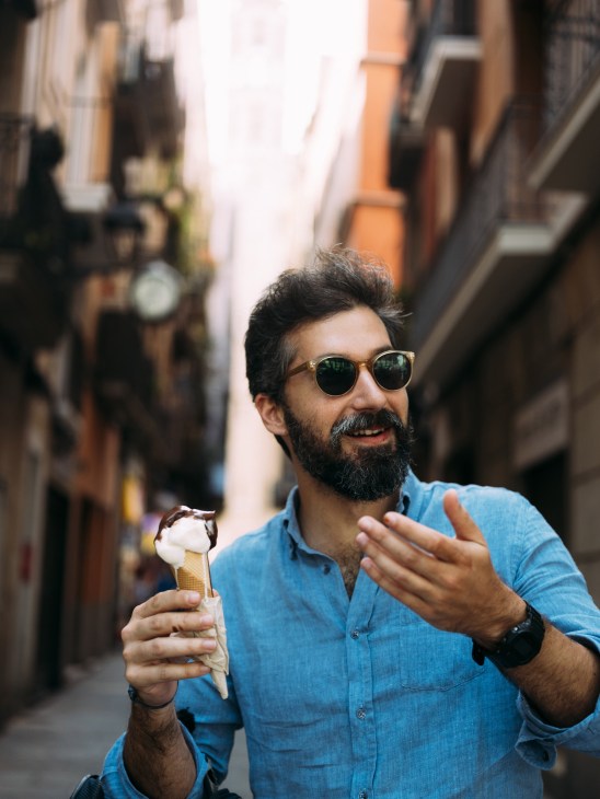 Man in blue shirt and sunglasses holding ice cream cone on Barcelona street