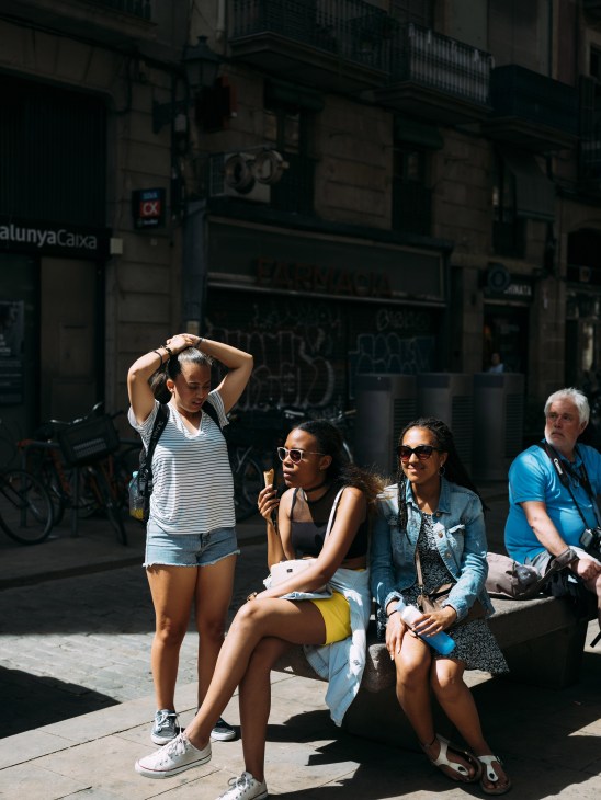 A group of tourists sitting on a bench in a Barcelona street enjoy ice cream on a sunny day.