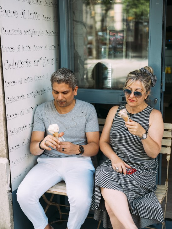 A man and woman sit on a bench outside an ice cream shop, each enjoying a cone in Barcelona.
