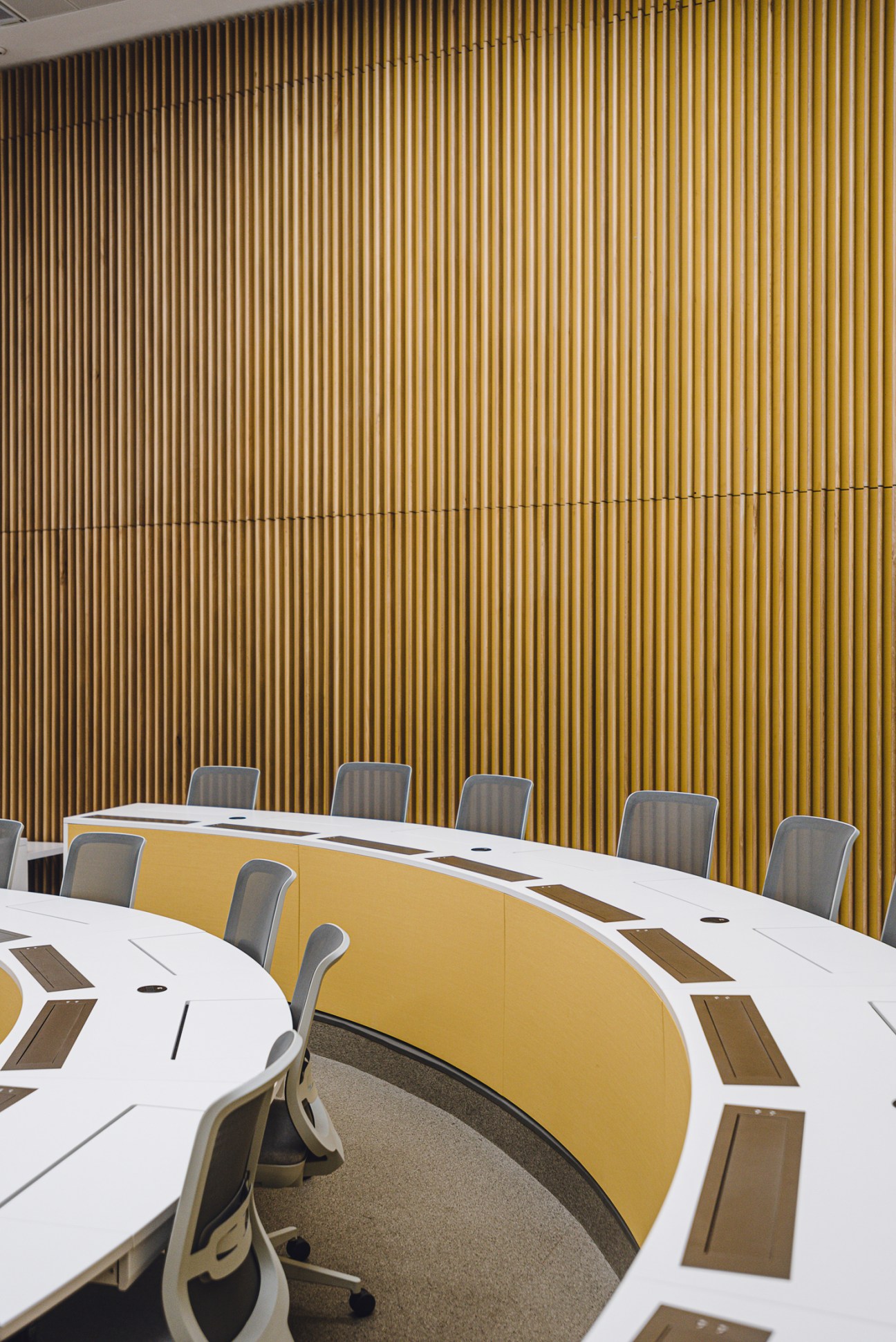 Modern conference room with curved white desks, gray chairs and vertical wood-paneled wall
