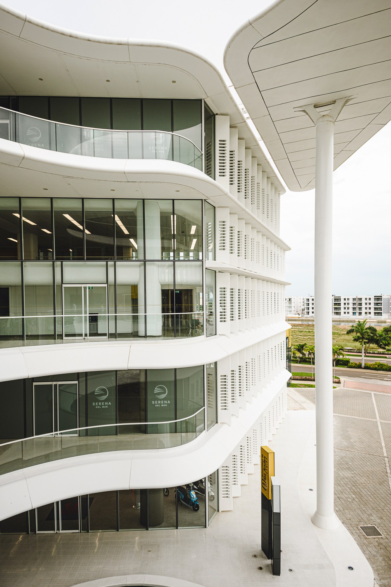 Modern university building with curved white balconies, glass facades, and white columns in courtyard