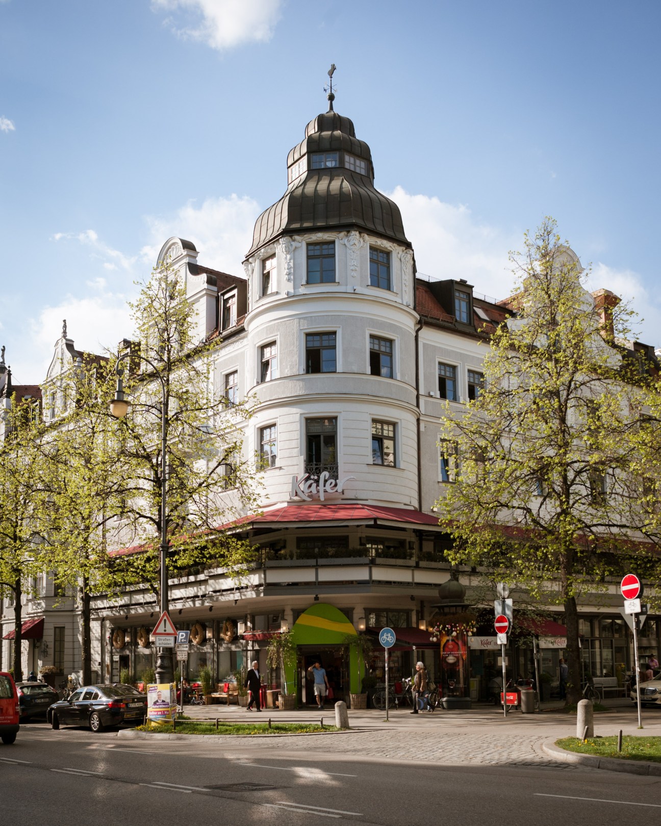 Historic white building with dome and red awning housing Käfer supermarket in Munich.
