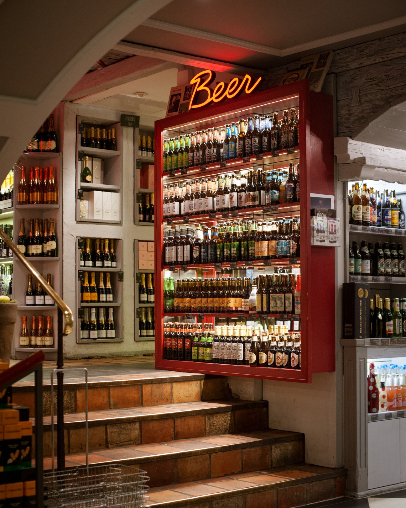 A red-framed beer display with neon sign at Käfer supermarket in Munich, showcasing various beer bottles on illuminated shelves.