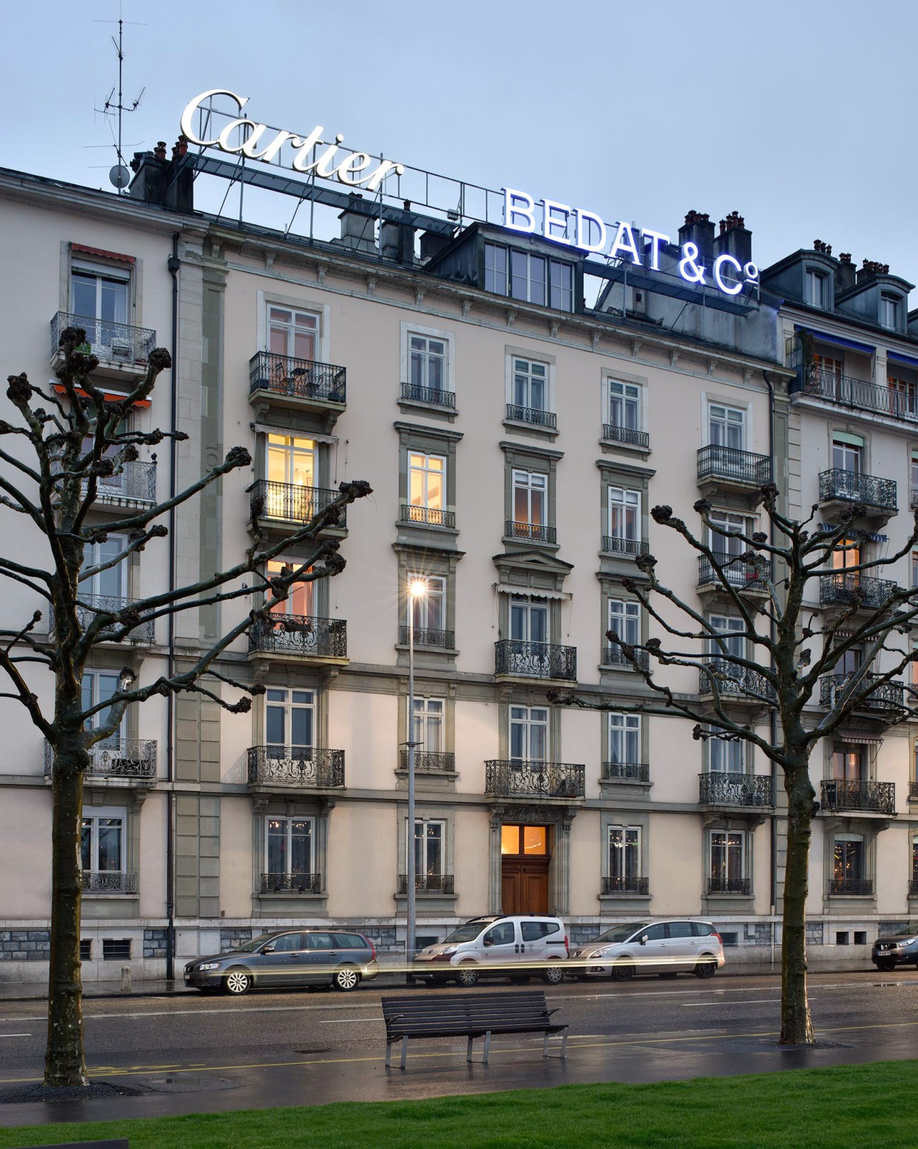 Historic building with Cartier and Bedat & Co neon signs illuminated on rooftop at dusk