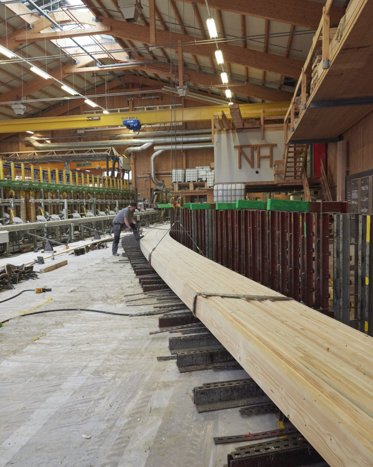 Worker bending large wooden beams in Neue Holzbau's industrial workshop facility.
