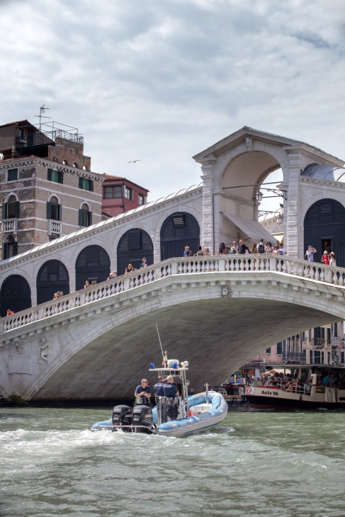 Police motorboat passing beneath Venice's Rialto Bridge with officers aboard
