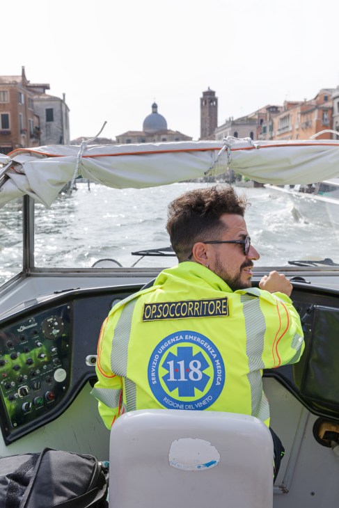 Emergency medical worker in neon yellow vest on ambulance boat on Venice's Grand Canal.