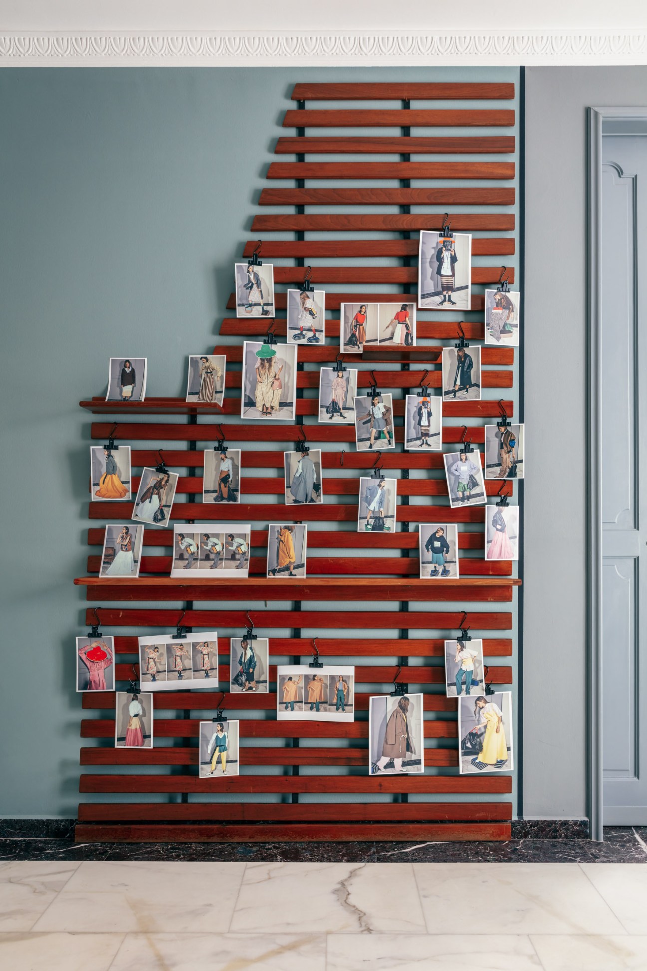 Fashion lookbook photographs clipped to a wooden slatted display rack on a turquoise wall.