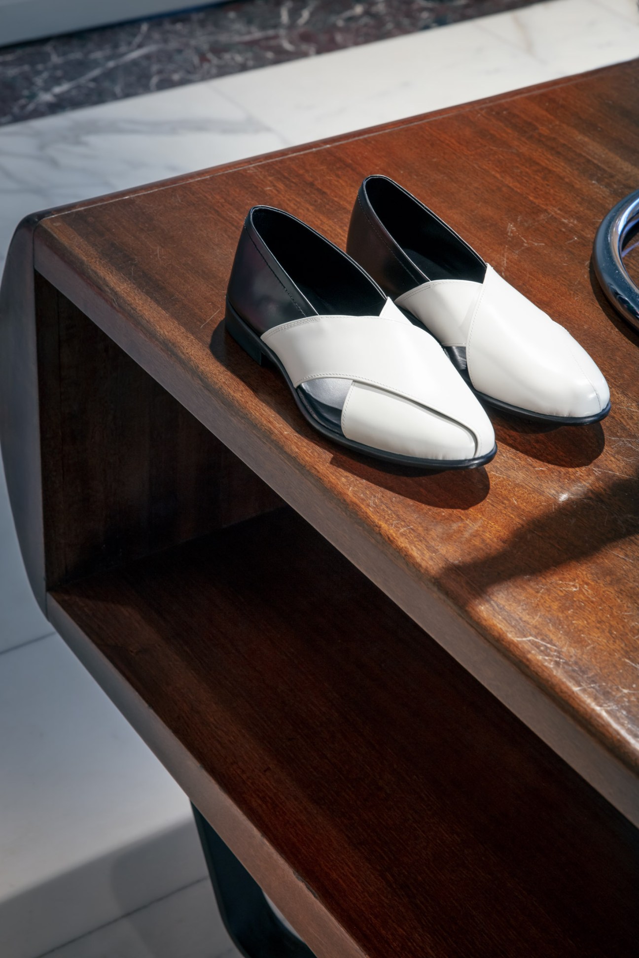 Pair of white and black leather slip-on loafers displayed on a wooden shelf.
