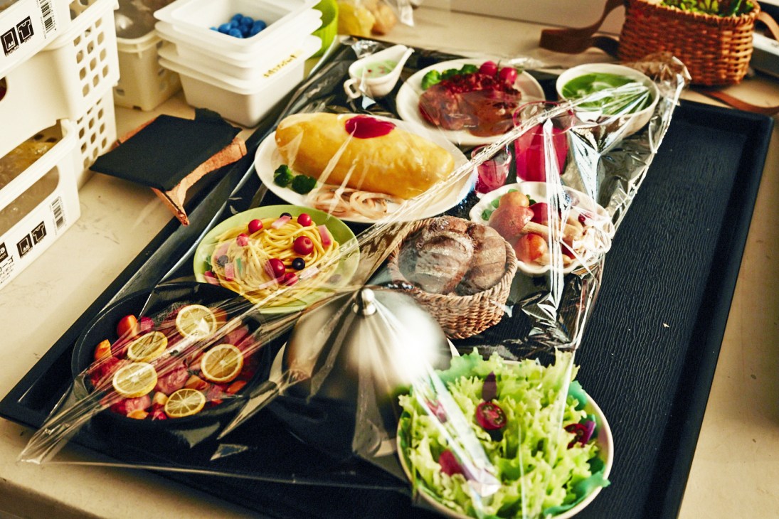 Miniature food props arranged on a table, including pasta, fish, meat, salad, and sliced lemons for stop-motion animation.
