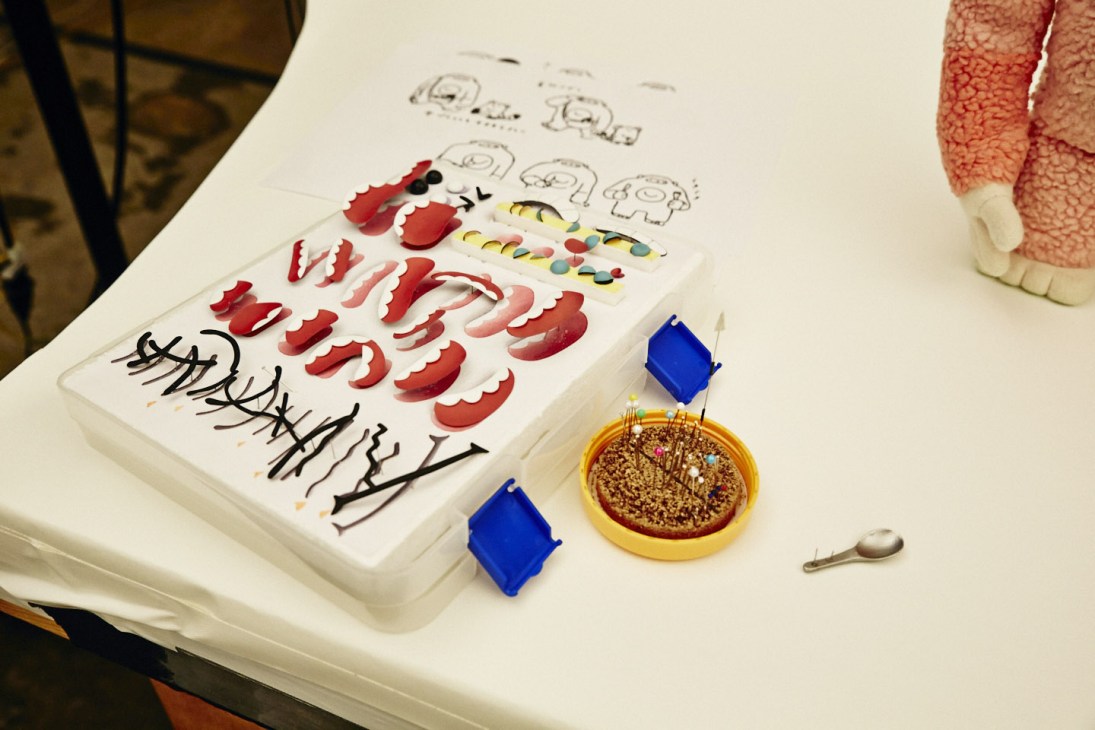 Replaceable puppet facial features including red mouths, eyes, and various expressions displayed on a white tray with character sketches.