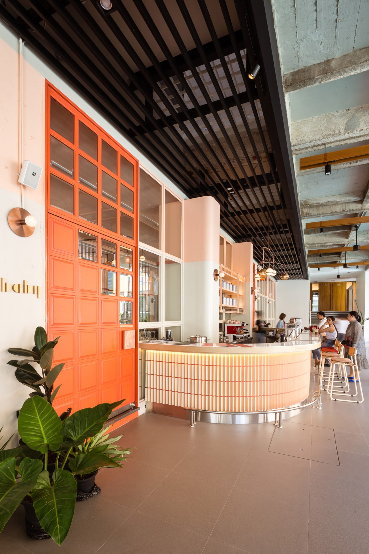 The Craftsman hotel cocktail bar in Bangkok with bright orange gridded doors, curved wooden counter and black slatted ceiling.