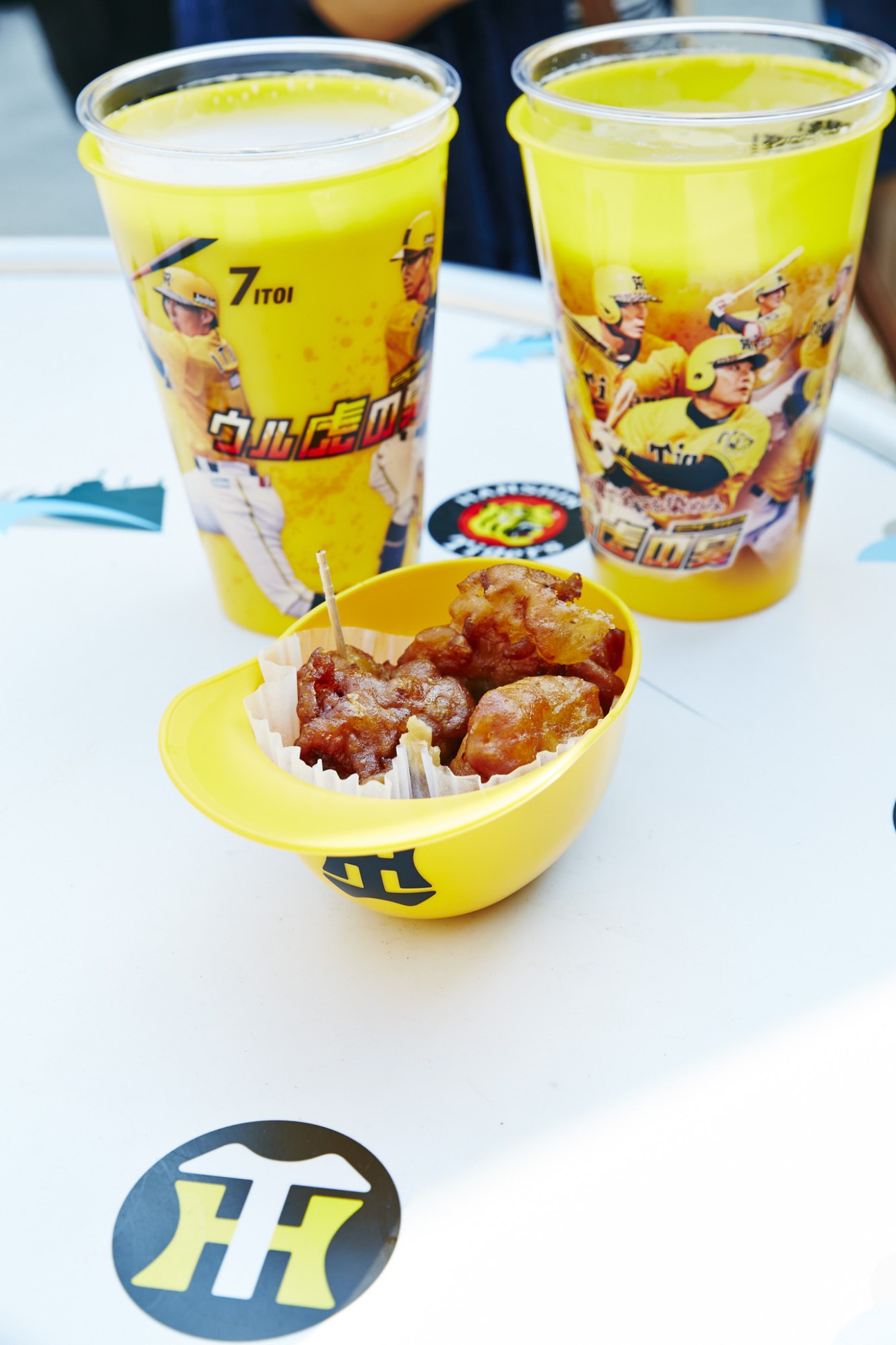 Yellow Hanshin Tigers branded cups with bright green beverage and fried chicken in a yellow bowl.