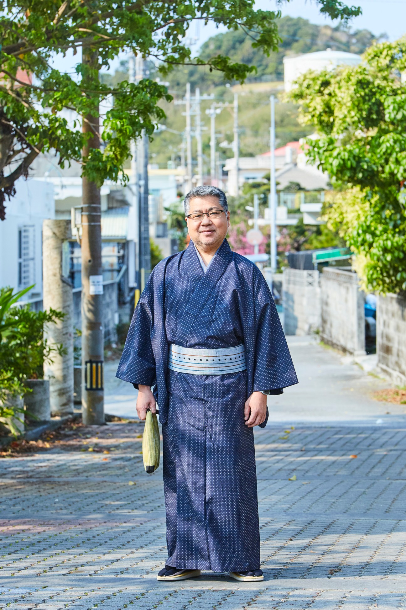 Satoru Oshiro wearing a traditional navy Ryukyu kasuri kimono while standing on a paved street