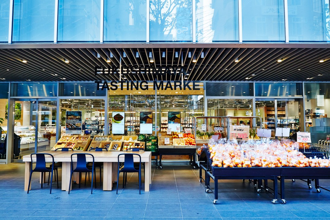 Fukushimaya supermarket storefront in Akihabara, Tokyo, with blue-tinted glass windows, wooden display tables with produce, and signage.