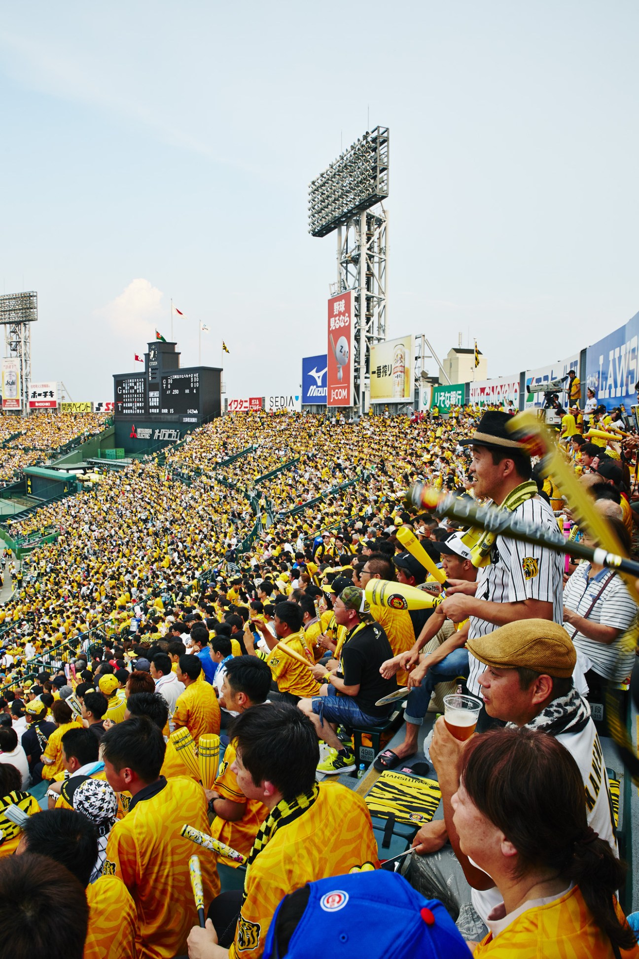 Packed Hanshin Koshien Stadium with thousands of fans in yellow and black cheering for the Tigers against the Yomiuri Giants.