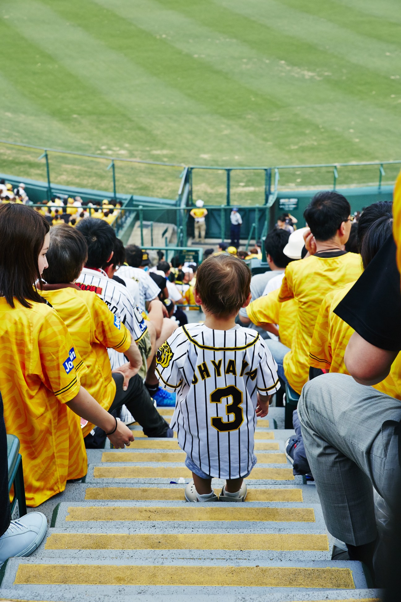 Young children in Hanshin Tigers yellow uniforms and pinstriped jerseys climbing stadium stairs.