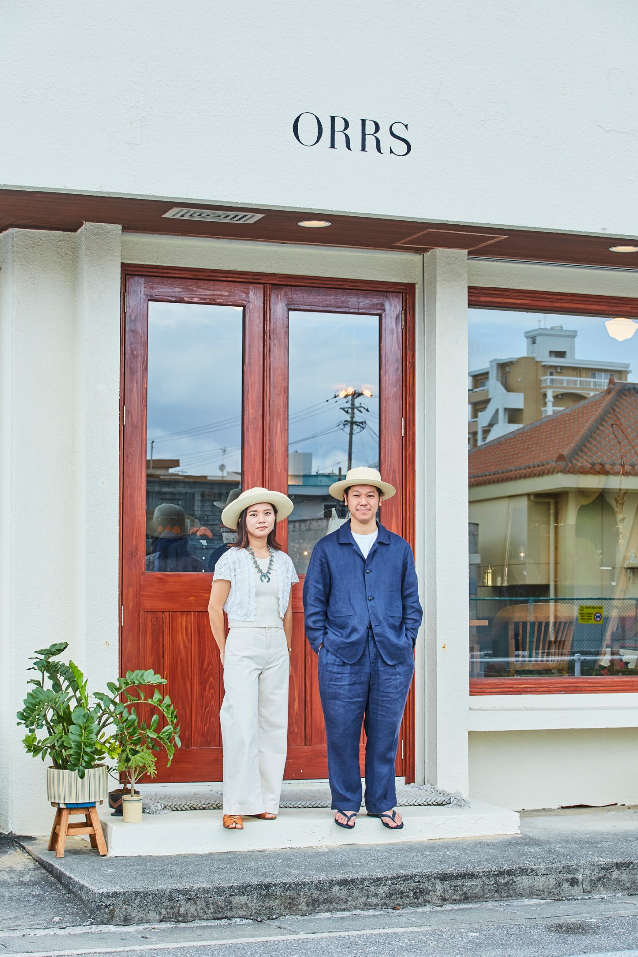 Wakako and Yosuke Sato standing in front of their Orrs menswear shop in Chatan wearing white and navy linen clothing