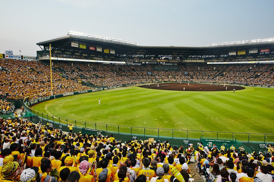Hanshin Koshien Stadium filled with thousands of yellow-clad fans in the stands during a baseball match.