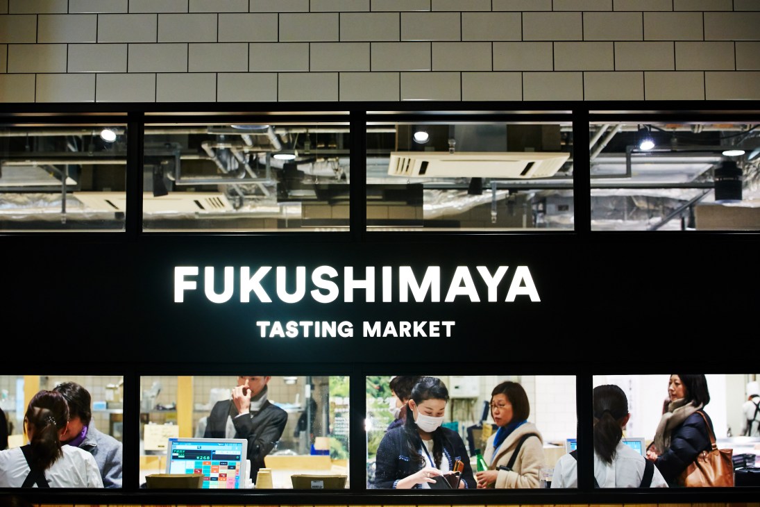 Fukushimaya Tasting Market storefront in Tokyo with illuminated signage and display windows showing customers and staff inside.