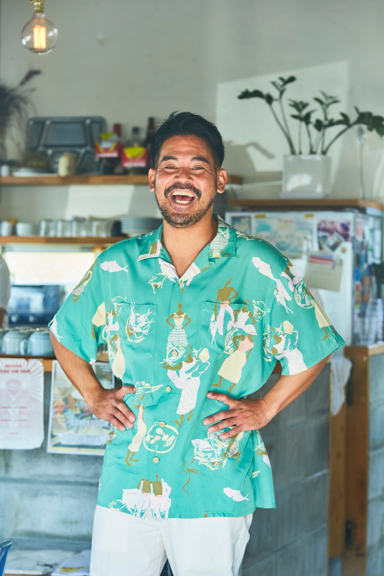 Tatsuya Miyazato, owner of Good Day Coffee, smiling in a turquoise Hawaiian shirt with hands on hips in his cafe