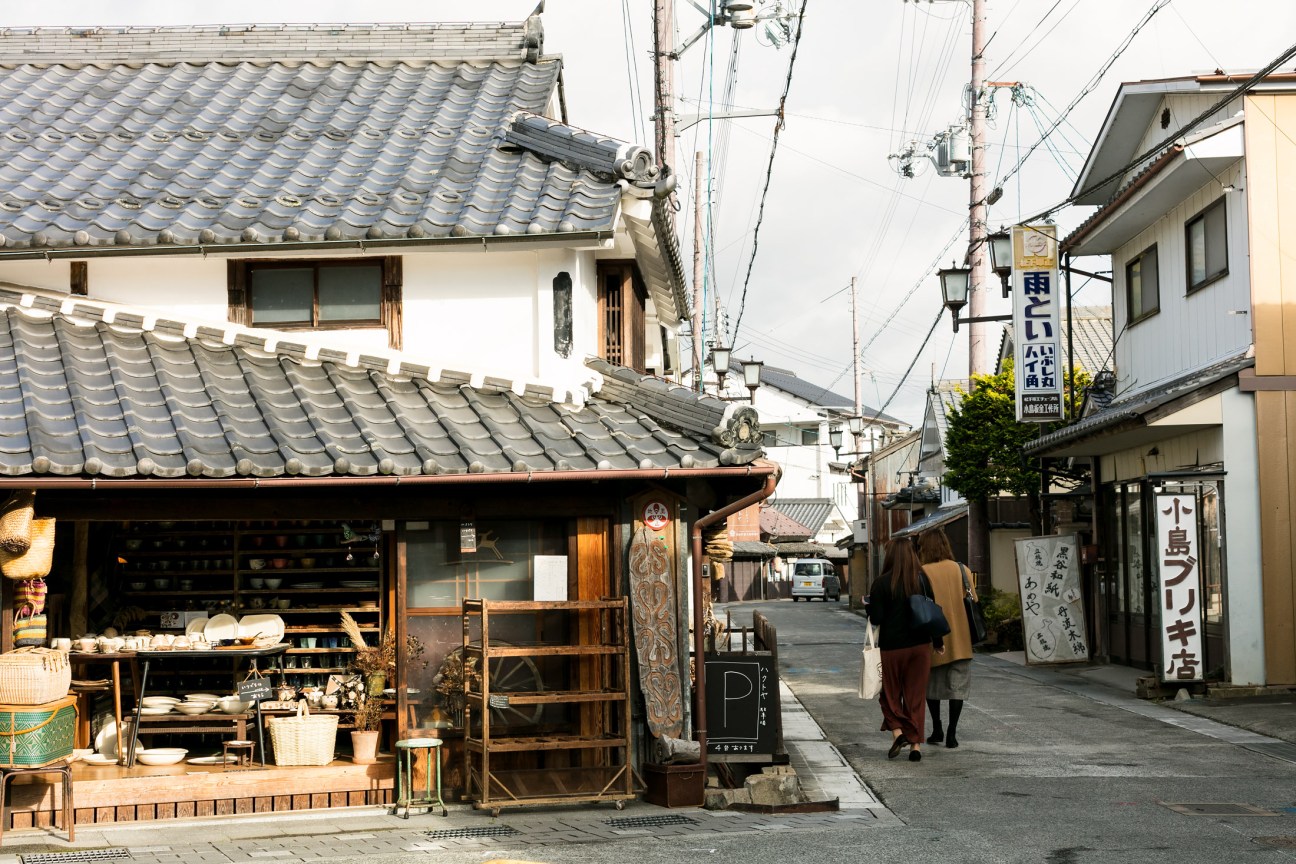 A traditional Japanese street in Sasayama with historic wooden buildings, tiled roofs, and a shopkeeper's storefront.