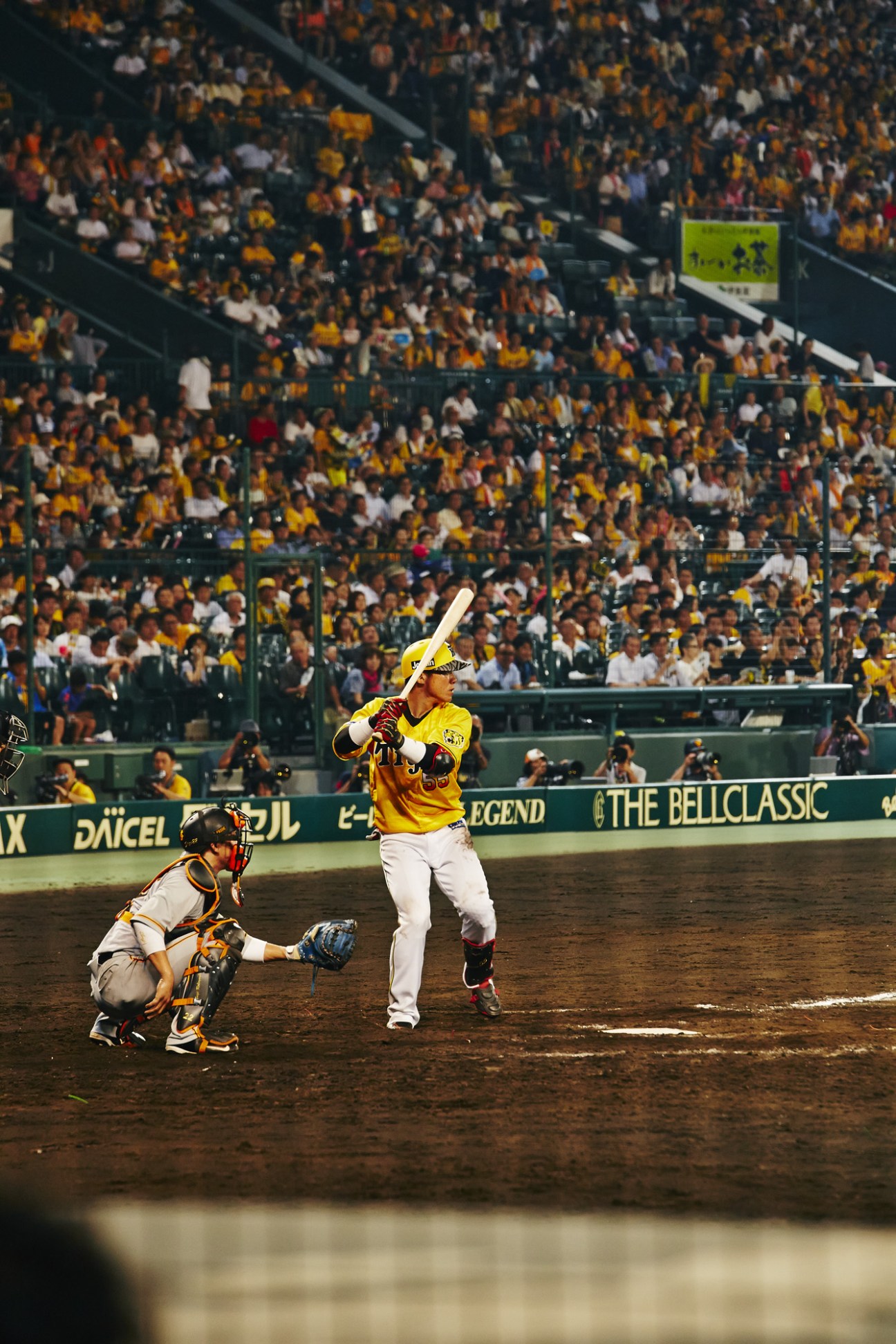 Hanshin Tigers player Naomasa Yokawa in yellow uniform at bat during game.