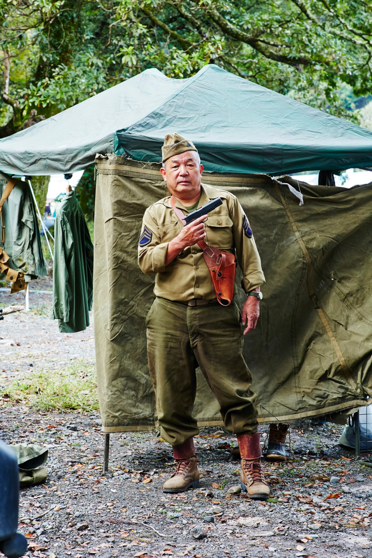 Person in military uniform standing next to military tent in outdoor setting