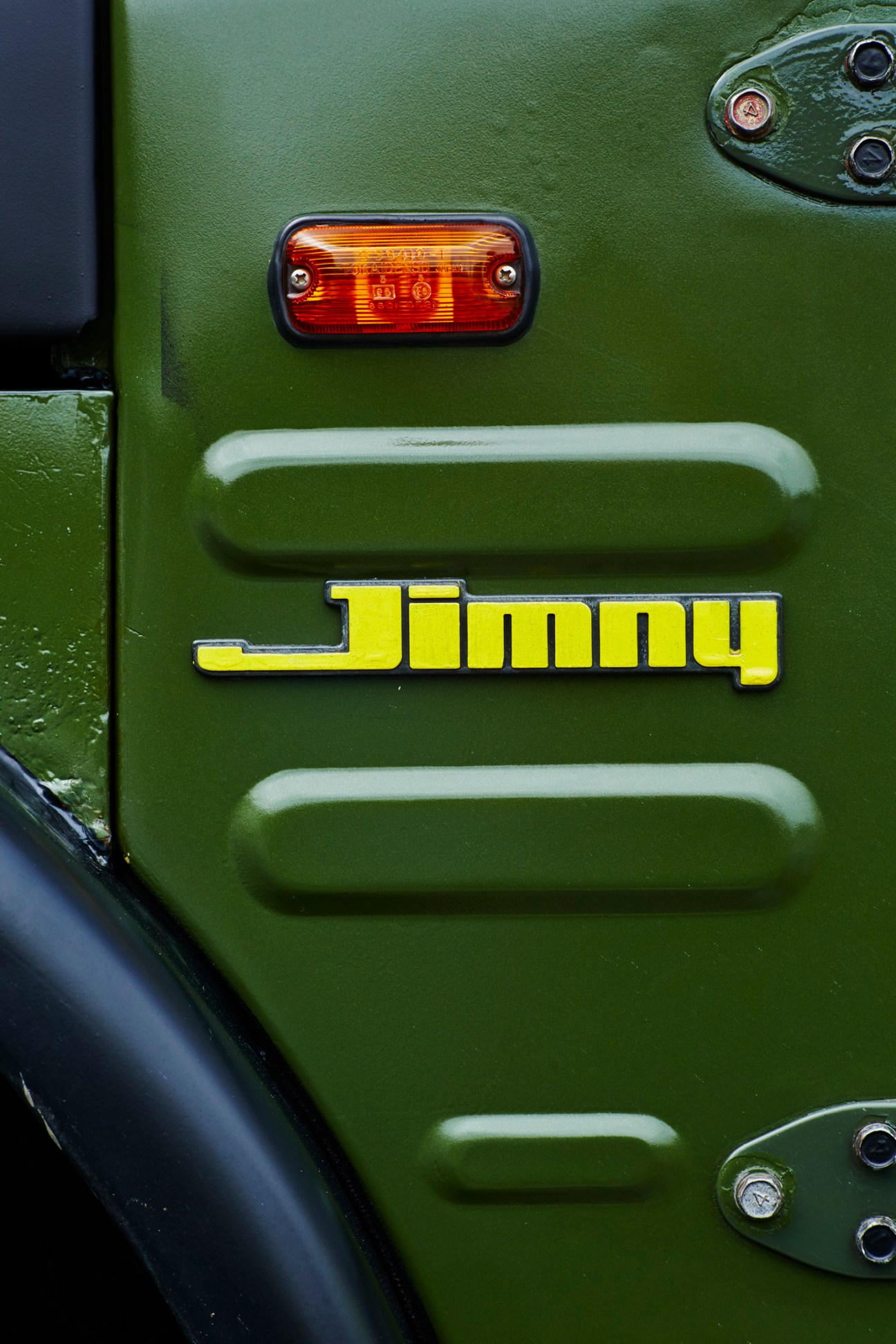 Close-up of green Suzuki Jimny rear panel showing yellow Jimny badge, side marker light and exterior door handle