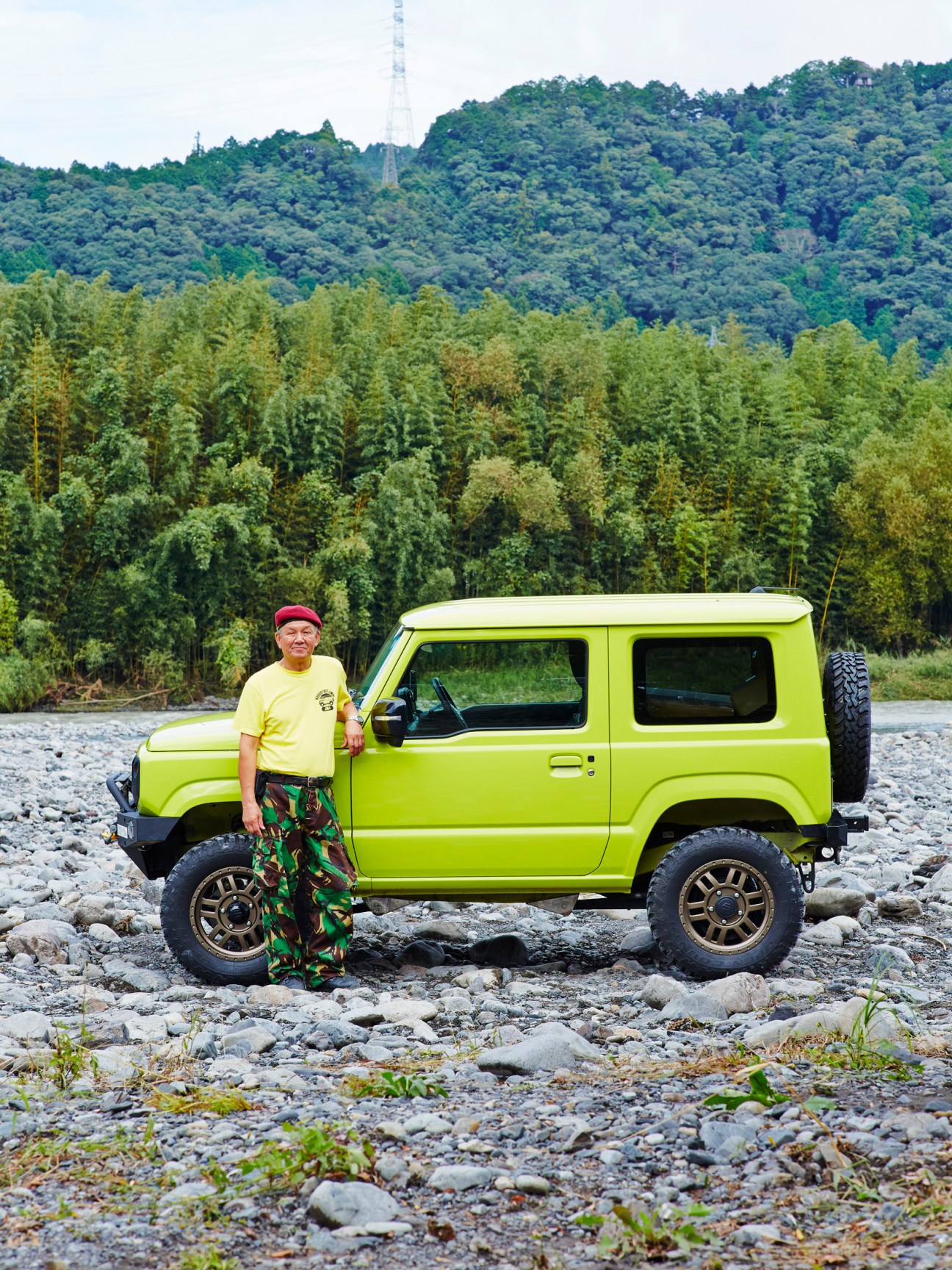 Yutaka Nikaido, chairman of Jimny Club of Japan, standing next to his bright yellow Suzuki Jimny on rocky riverbank