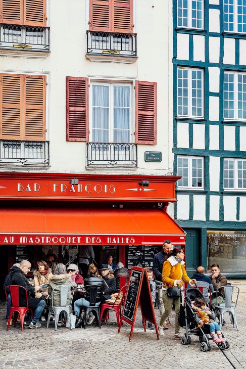 Outdoor café seating in front of red storefronts with traditional European architecture in Bayonne.