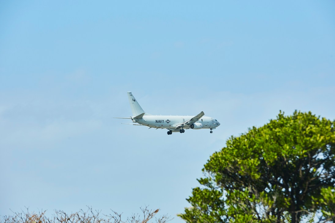 US Navy aircraft flying above green trees against blue sky near Kadena Air Base in Okinawa