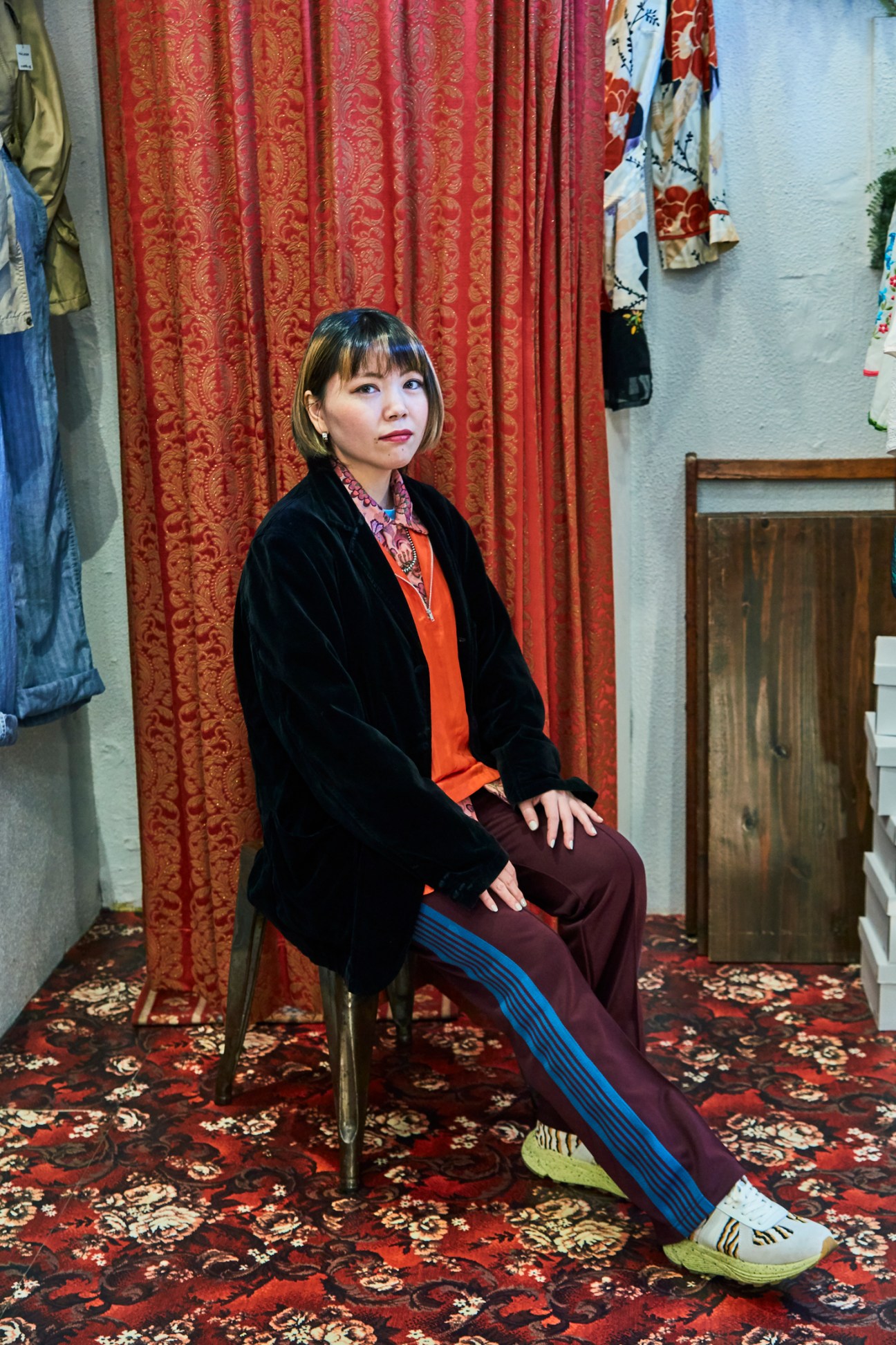 Riya Shimabukuro sitting on a chair wearing layered clothing by Noma and Needles brands