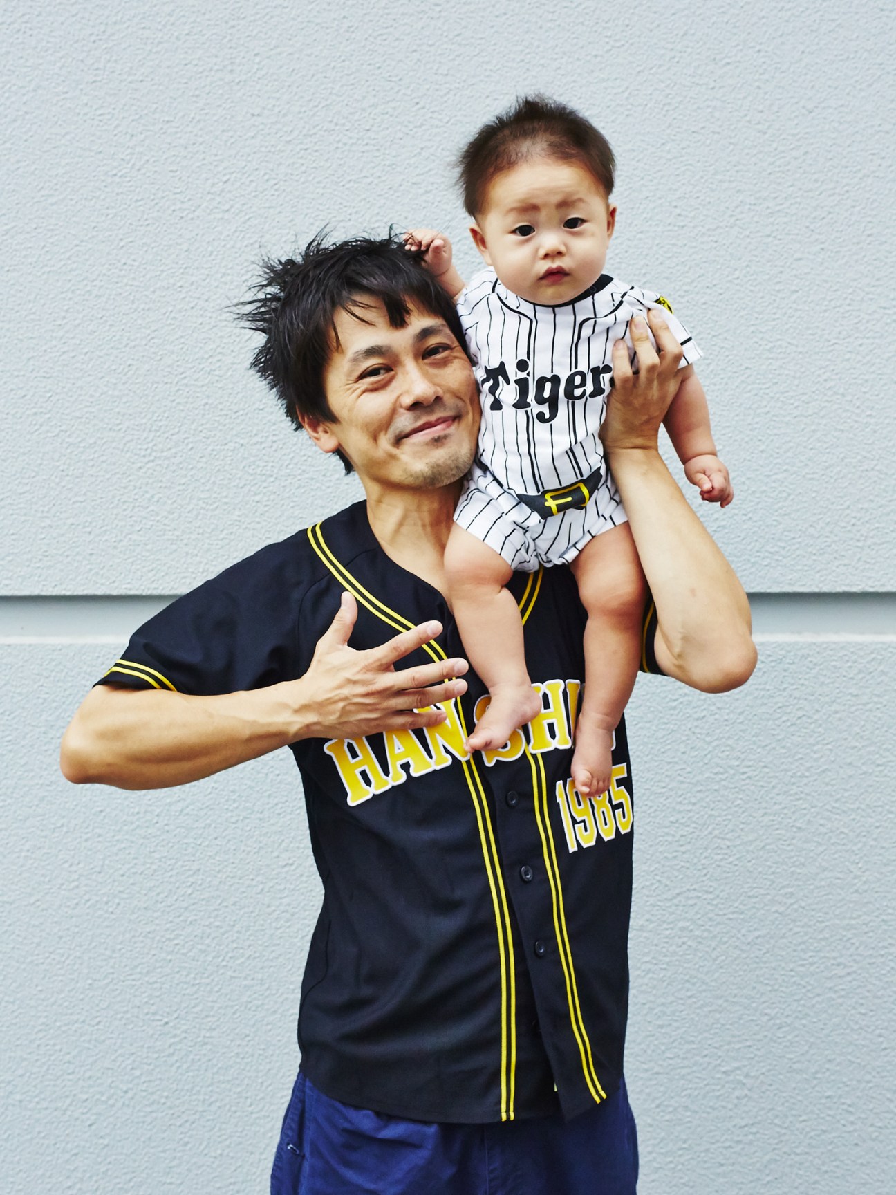 Adult man holding young child wearing Hanshin Tigers baseball uniforms.