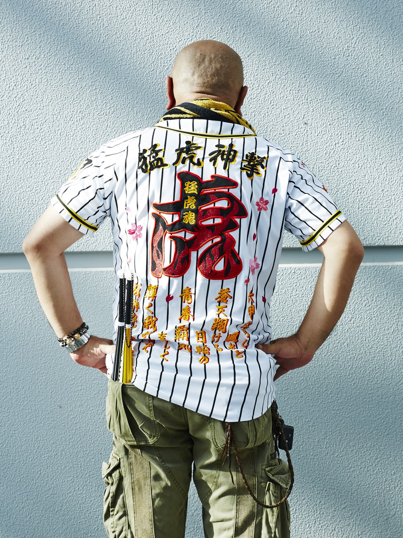 Man wearing white pinstriped Hanshin Tigers baseball uniform with Japanese characters and red tiger logo on back.