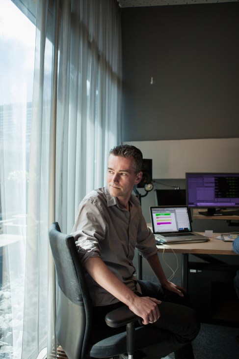 Man seated at desk by window with laptop displaying colorful data visualization in modern office.