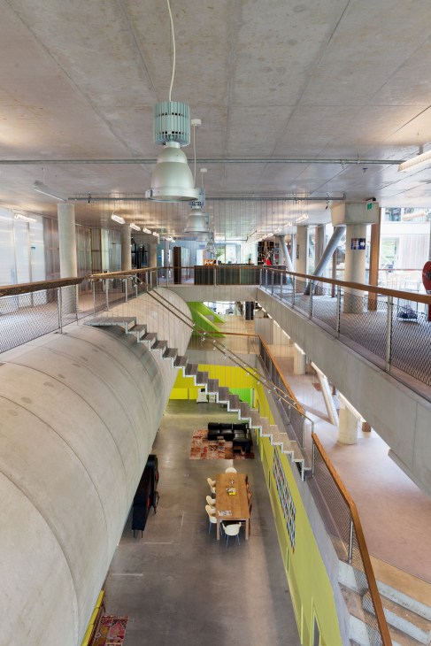 Interior view of VPRO office in Hilversum showing multiple levels with concrete ceilings, metal railings, and bright yellow accent walls.