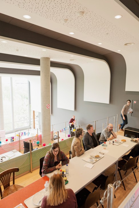 VPRO staff members seated at a long table during lunch in a modern office space with industrial design elements.