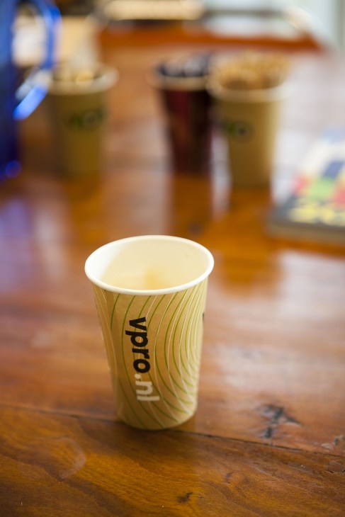 A branded VPRO coffee cup filled with light-colored beverage on a wooden table.