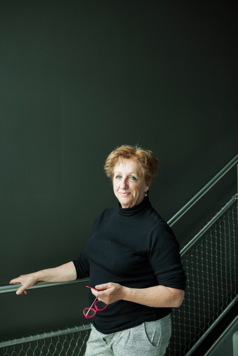 Nel Koopman, a VPRO employee of 40 years, poses against a green wall next to metal stairs.