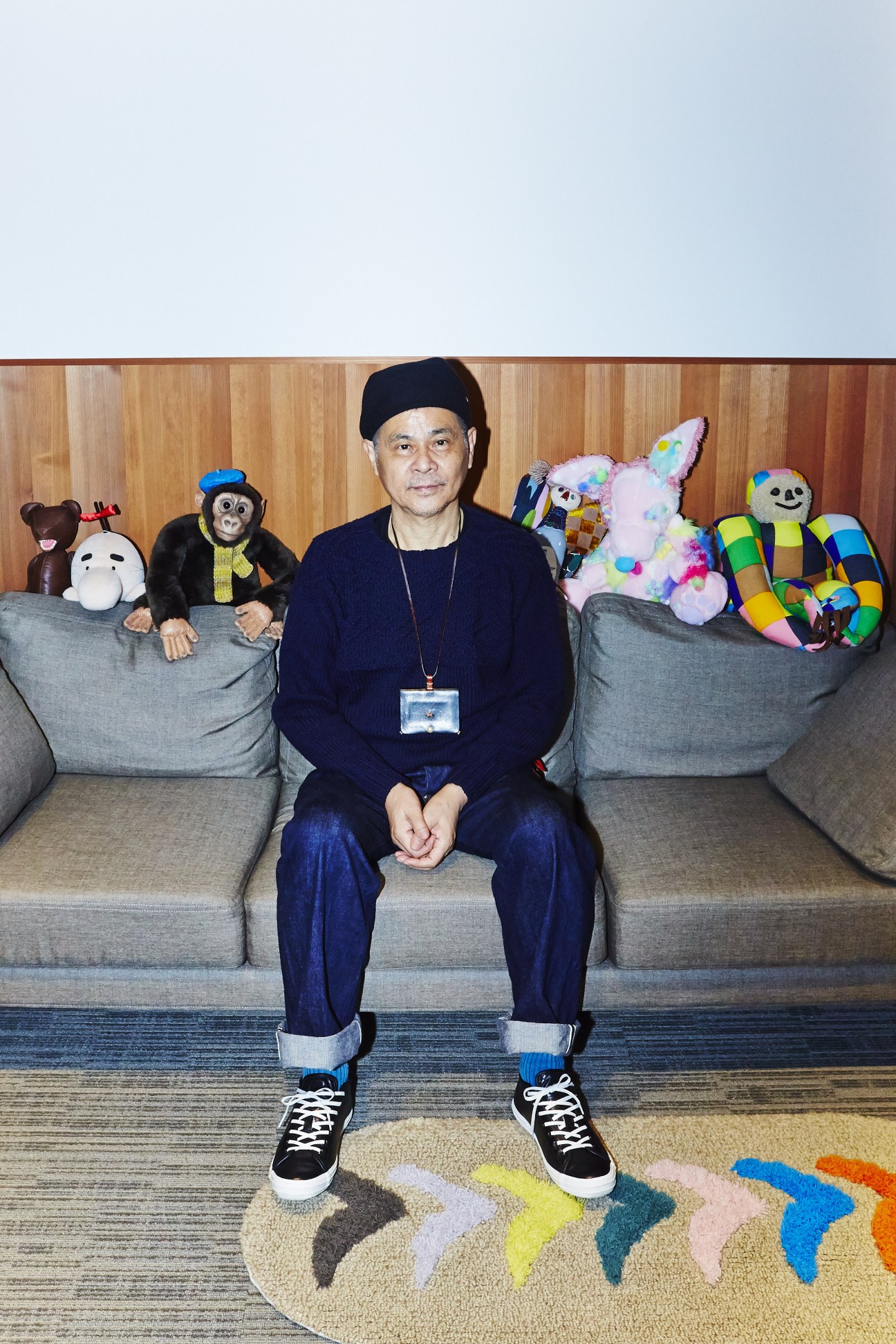Shigesato Itoi sits on a couch surrounded by colorful toys and stuffed animals at Hobonichi headquarters.
