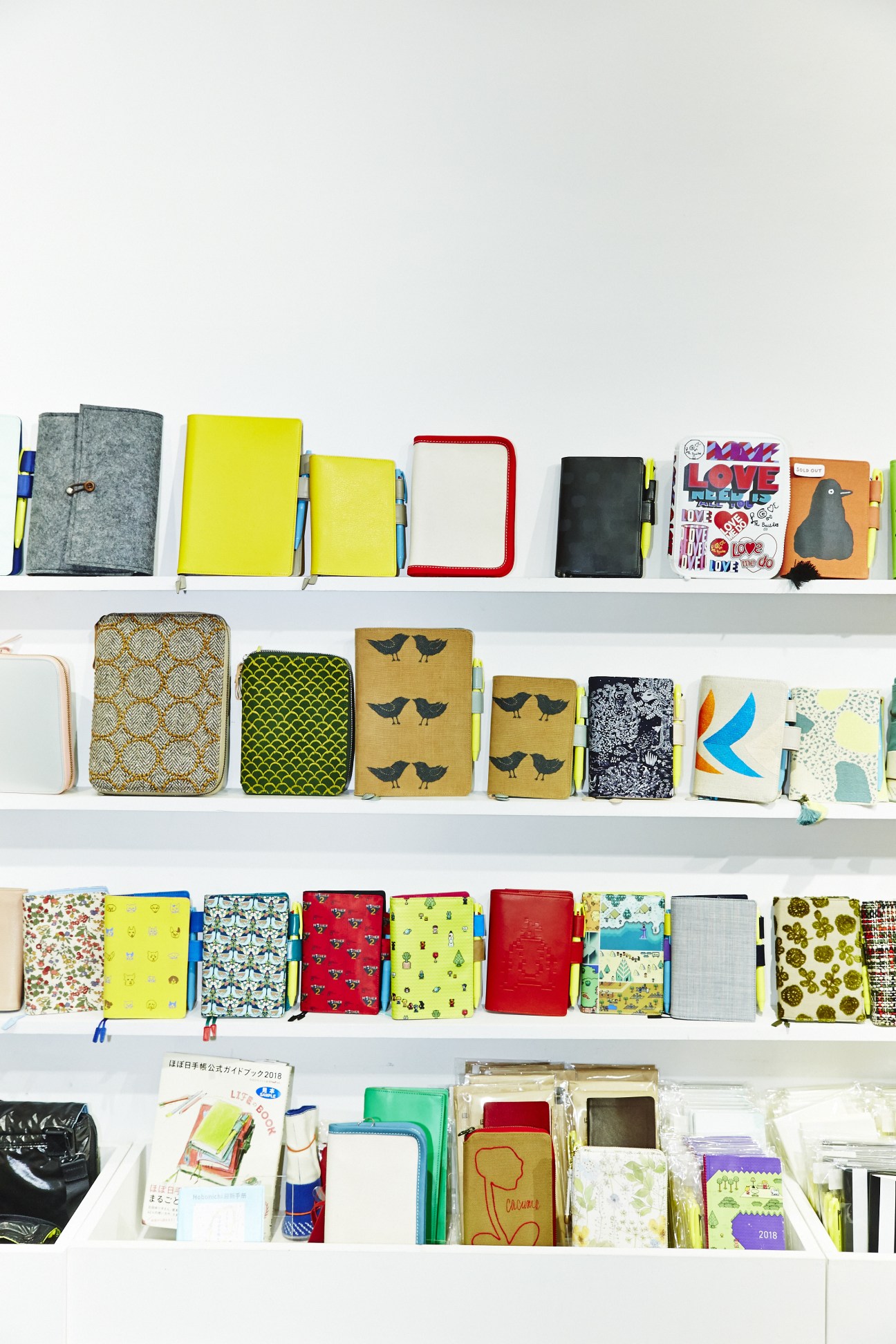 Colorful Hobonichi Techo pocket-book planners displayed on white shelves.