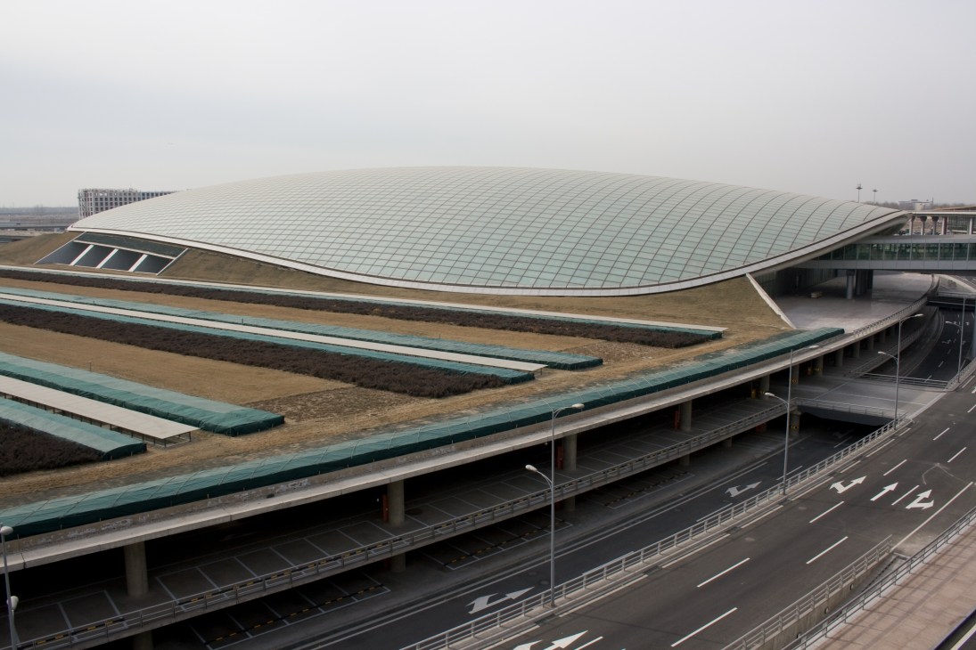 Modern curved metallic roof structure of Beijing airport train station with highway below.