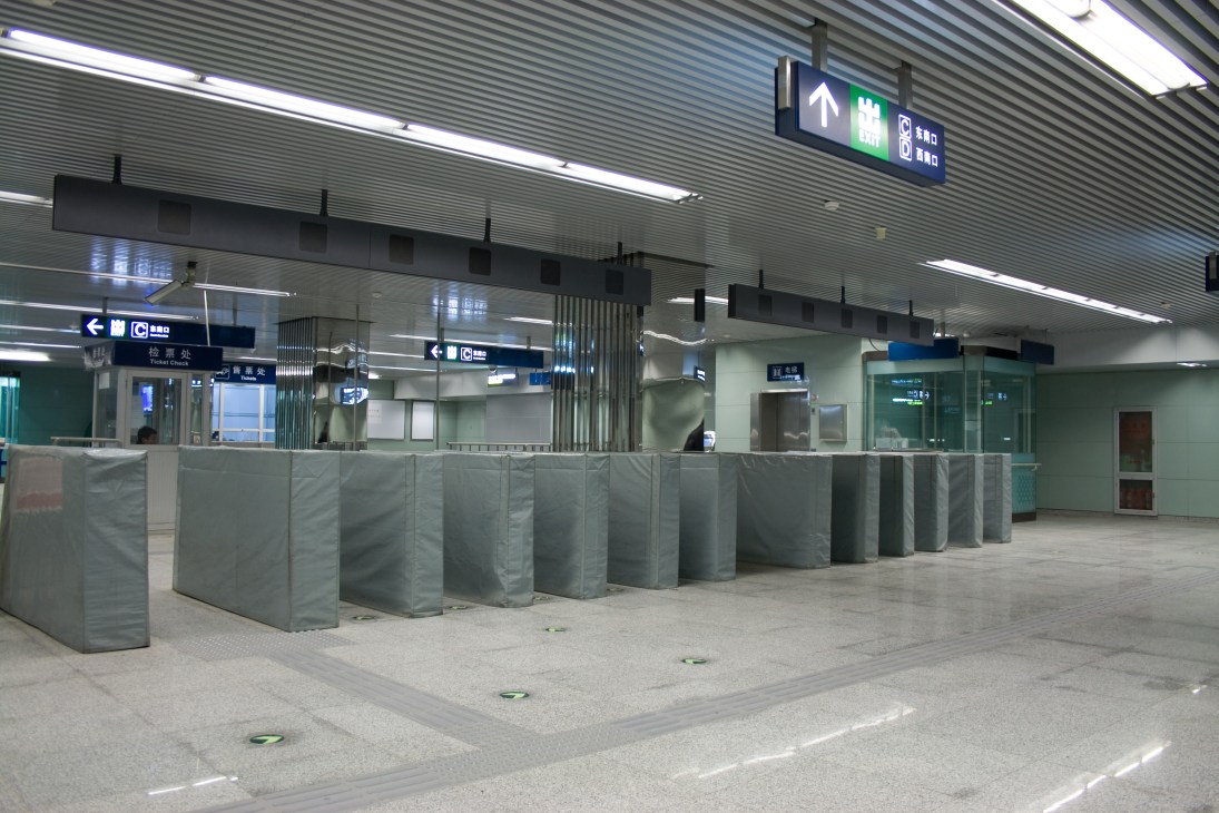 Modern Beijing subway station interior with ticket booths, directional signage, and fluorescent lighting.
