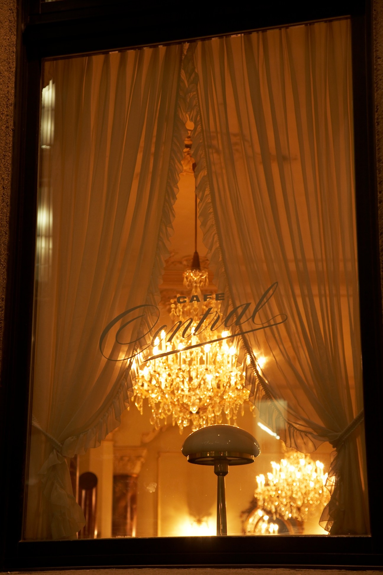 Café Central storefront with glowing chandeliers and gold curtains visible through window at night